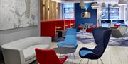 Lobby in Holiday Inn Express Belfast City. Blue and red chairs, coffee table and grey sofa in the foreground, with map of Belfast on the