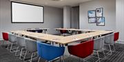 Meeting room in Holiday Inn Express Belfast City. The room is in U-shape style with stylish red, blue and grey seats. Tables are set with c