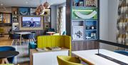 Photo of the lobby in Holiday Inn Belfast City Centre. Tables with colourful chairs, TV screen in the background. Wall unit with colourful niches with
