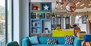 The lobby in Holiday Inn Belfast City Centre. Blue sofa with coffee tables in the foreground. Wall element with colourful niches with decor