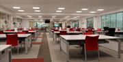 Interior photograph showing the PRONI Reading Room with a dozen tables and red chairs placed at each table.