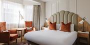 Contemporary hotel bedroom with king-size bed, statement headboard, seating area and soft neutral décor.