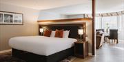 Spacious hotel suite featuring a king-size bed, separate lounge area and large windows with natural light.