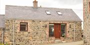 Image shows front of stone cottage with wooden door and gravel driveway.