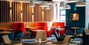 Open lobby in Holiday Inn Express Belfast City. Booths with colourful seating, colourful chairs and tables, wood panelled back wall and m