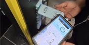 A customer holding a PLUGINMOVE portable power bank beside a PIM infrastructure asset while using the PLUGINMOVE mobile app to view nearby rental loca